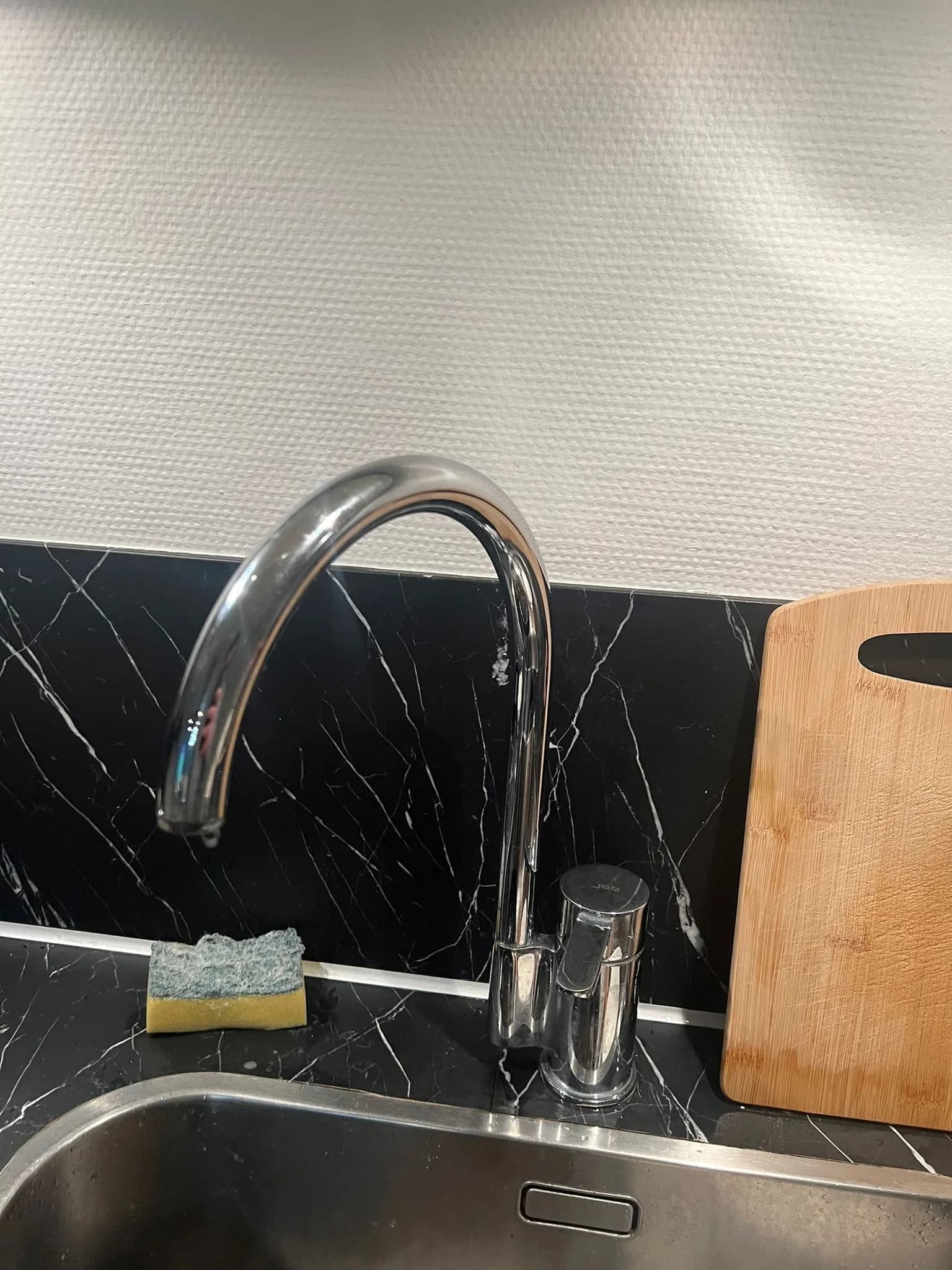 Verchroomde keukenkraan op een zwart marmerlook achterwand