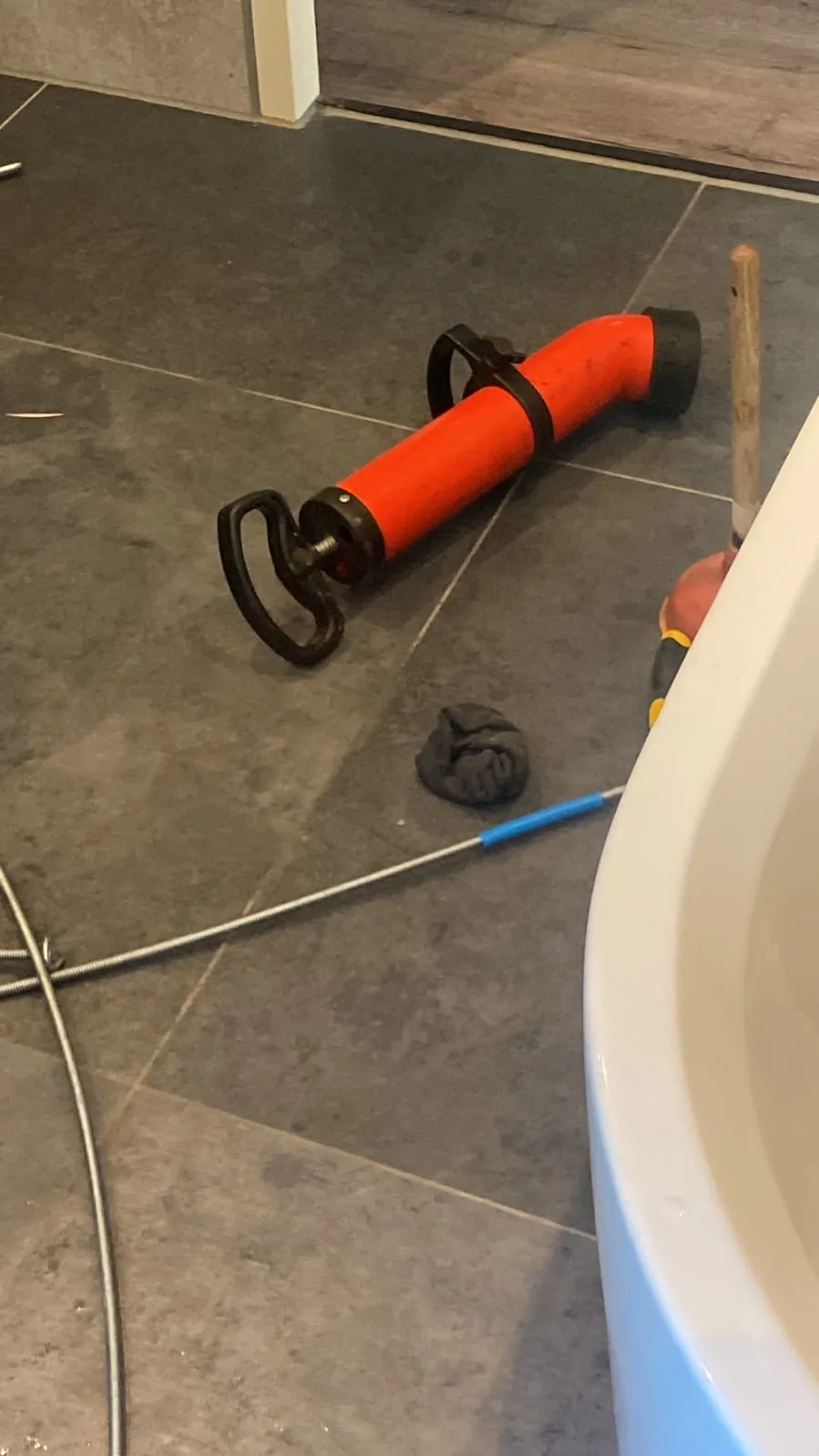 Ontstoppingspomp en afvoerveer naast het bad tijdens het ontstoppen
